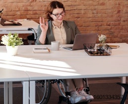 woman in wheelchair sitting at a table looking at her computer